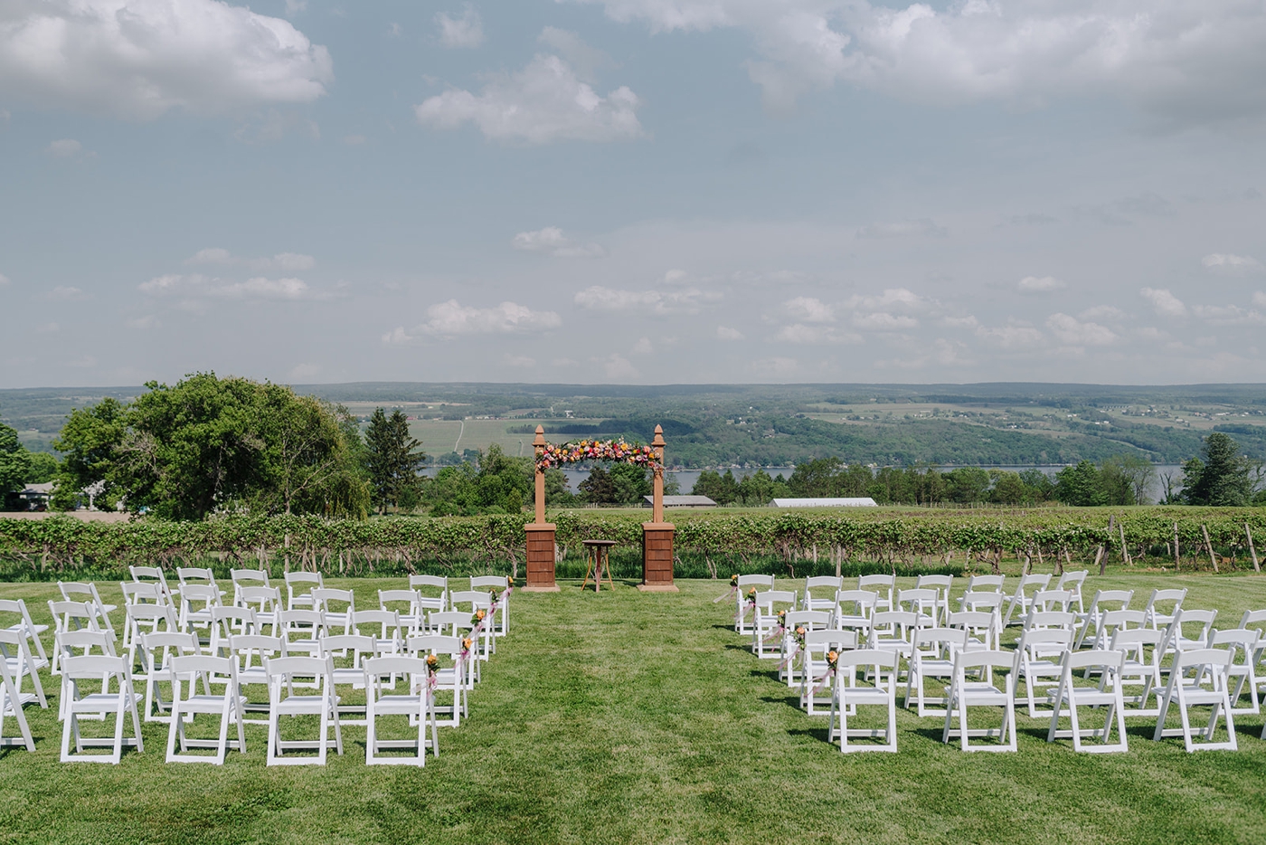 White folding chairs, a wooden archway, and pink and orange florals for a spring wedding ceremony