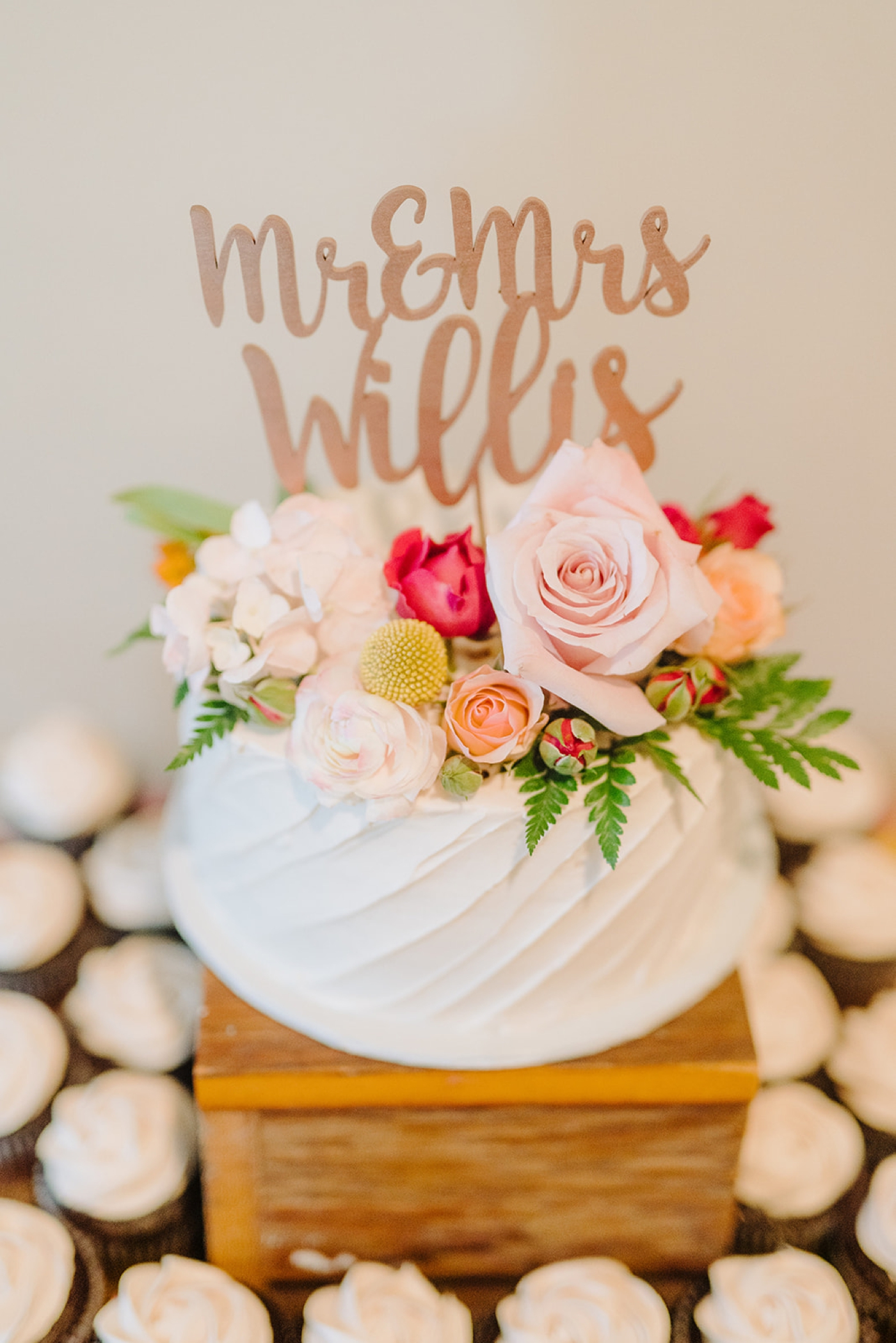 Spring wedding cake decorated with a rose gold topper, blush roses, and ferns